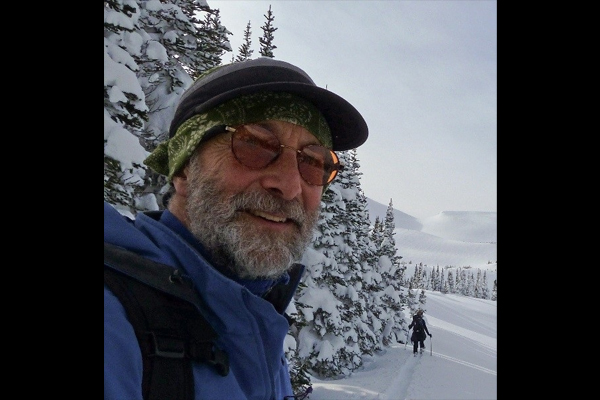 Peter smiling in mountaineering gear on a snowy slope. He has a full grey beard.