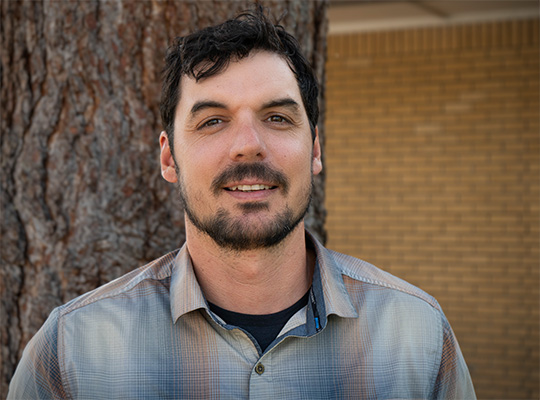 Head shot of man with black hair, smiling at the camera.